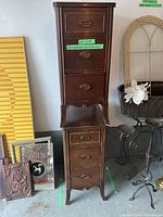 Pair of dark wood night stands stacked vertically in a storage area, showing drawer handles and legs.