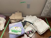 Photo of assorted queen size sheets in various colors including cream, white, and floral patterns alongside packaged sheet suspenders.