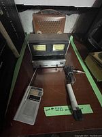 Photo showing Realistic Audio Power Meter, portable radio, and handheld microphone on a table with a leather carrying case in background