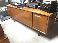 Photo showing full wood cabinet with three sliding front panels and items on top, placed in basement area.