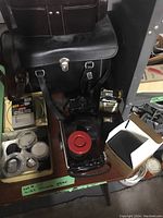 Wide view of camera bags, filters in tin container, red lens flash, and boxes on a wooden table.