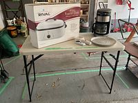 Photo showing folding camping table holding coffee maker, roaster oven box, pie plate, and magnifying glasses.