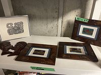 Photo of 3 framed silk thread art pieces and 1 framed aboriginal ink print, plus 2 carved wooden wall art pieces on table with concrete wall background.