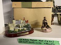 Photo showing miniature replica of Sintra castle, small bronze seated female statue, with a beige box in the background and a note describing the lot items including fedora hat and cat hook rack.