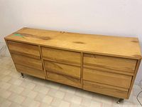 Front view of the light wood 9 drawer dresser showing stains and general worn condition.