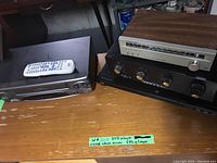 Photo of AM/FM stereo tuner with wood finish stacked on other stereo equipment and JVC DVD player with remote on left side of table.