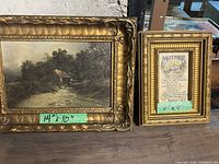 Two framed art pieces on a shelf. Larger 14x10 inch framed landscape painting depicting watermill by a river surrounded by trees. Smaller 7x9 inch framed poem titled 'Mother' with floral design.