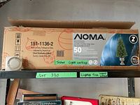 Shelf showing original box of NOMA lighted potted pine tree with 50 lights, and attached light timer unit.