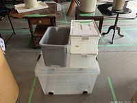 View of four stacked plastic containers including large clear container with wheels, medium gray container, and two small clear containers with beige lids
