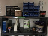 Metal shelf with various hardware items including bins of nails, containers, and spray paint.