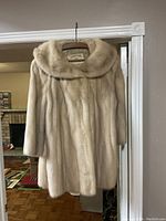 Full view of the blonde mink fur coat hanging showcasing its length and wide collar.