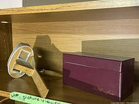 Vintage handheld picture viewer made of wood and metal, placed on a shelf with a burgundy box beside it.