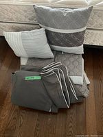 Photo showing queen size bedding set items including comforter, bed skirt, two shams, two pillowcases, and two cushions arranged on wooden floor