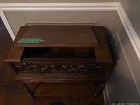 Closed wood side table with ornate carved front and hinged lid on top.