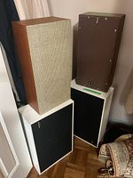 Four speakers arranged, two with maple wood cases and fabric front, two with white casing and black fronts, one showing Realistic badge.