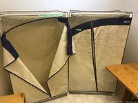 Two beige cloth wardrobes with black trim, one partially unzipped to show interior.