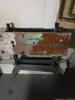 Used folding work bench with wooden top showing paint marks, scratches, and holes, with metal foldable black legs below.