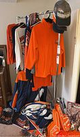 Full lot display showing various Denver Broncos apparel hung on rack, blankets on floor, a foam finger, and Broncos memorabilia.