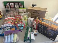 Overview of lot showing various new items in original packaging including candles, toys, and personal care products