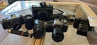 Lot of various cameras and lenses arranged on glass table