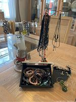 Wide arrangement of costume jewelry on and around a clear stand including bracelets, cuffs, necklaces, and earrings.
