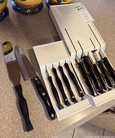 Two knife sets in white storage cases with two loose utensils on countertop