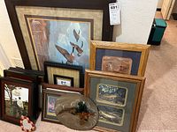 Framed wildlife and family-themed art pieces arranged on carpet, featuring scenes of ducks, fishing, and countryside.
