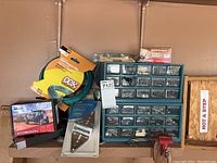 Photo showing small parts organizer with screws, 3-inch D-ring shackle in box, roll of garden wire, metal hardware bracket, and small red vise