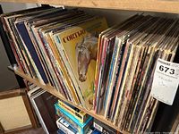 Side view of a shelf holding over 50 assorted jazz and disco LP records in cardboard sleeves, upright on shelf.