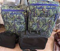 Two purple and green paisley pattern rolling luggage pieces with front zippered pockets and silver-tone locks, two black bags in front.