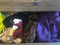 Drawer view showing assorted neon yellow top, beige pouch, black faux fur scarf, burgundy and white fuzzy socks, brown faux fur accessory, purple knit sweater.