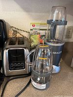 Nutribullet blender base with two blending cups, KitchenAid toaster, recipe book on kitchen counter