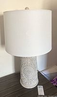 Pair of white table lamps with embossed ceramic bases and white fabric drum shades, photographed on a wooden surface.