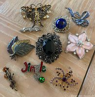 Full view of the lot showing 9 assorted pins and brooches on a wooden surface.