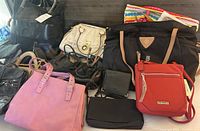 Overhead view of assorted purses and bags laid out on a surface including a pink handbag, a black tote, a white handbag, and a red crossbody bag.