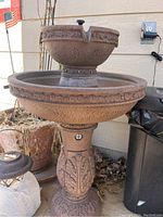 Two-tier brown decorative outdoor water fountain with ornate patterns and water spout on top.