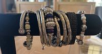 Front view of 5 bracelets including metal twisted cuff with silver ends, silver wide cuff with textured pattern, beaded bracelets with natural colored beads and silver accents.