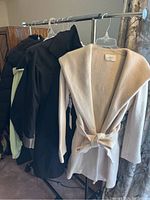 Rack with four women's coats: a beige Wilfred A coat with belt, black formal coat, black puffer jacket, and a light green jacket.