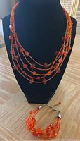 Orange multi-strand beaded necklace and matching bracelet displayed on a black jewelry stand.