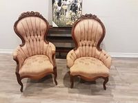 Front view of two pink Victorian-style upholstered chairs with carved wooden frames, showing tall rounded backs, padded armrests, and floral upholstery.