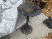 Full view of the cast iron bird bath showing the scalloped edge basin and decorative circular base on tiled floor outdoors.