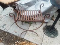 Cast iron garden bench showing full front and side view on tiled floor with other iron furniture parts nearby.