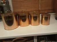 Front view of four copper canisters in different sizes with lids on a white countertop.