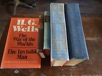 Front view of five H.G. Wells books showing various sizes and colors from modern orange dust jacket to old blue hardcover editions.
