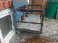 Side angled view showing metal frame, wooden slats base and castors of the old factory cart.