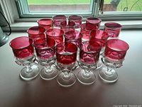 Front and top view of 15 ruby red wine glasses arranged on a white surface near a window showing details of color and texture.