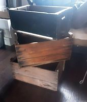 Three stacked wooden crates showing various wood finishes and one black painted crate on top.