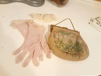 Photo showing embroidered handbag, pink gloves and lace garter laid on table.