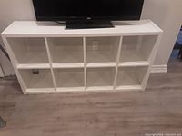 White cubby storage unit or TV stand with a TV placed on top, showing ten open cubby-style storage compartments arranged in two rows of five each.