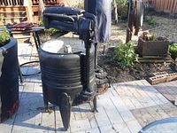 Full view of the vintage cast iron wringer washer converted into a planter, showing the cylindrical tub and wringer rollers with crank arm.